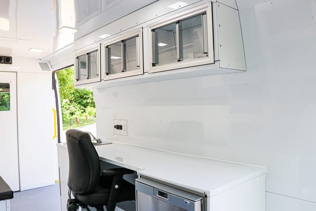 Mobile Medical Clinic Van office space with upper cabinets, desk space, fridge, sink, and chair